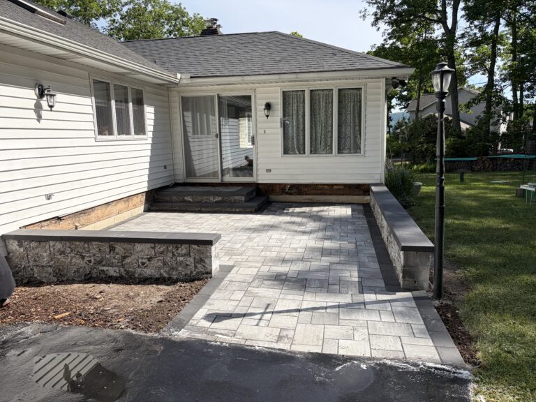 Finished gray paver walkway leading to a raised patio and front steps